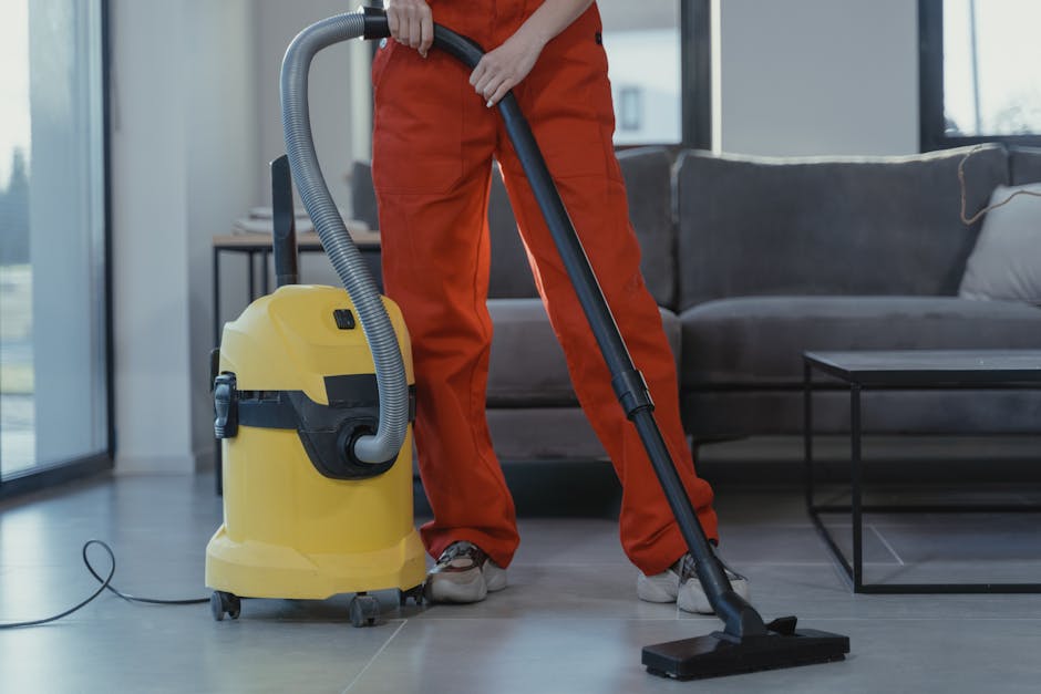A team of three professional cleaners from Dulwich Cleaner are engaged in surface cleaning and deep cleaning tasks inside a modern living room. The room features a light-colored tiled floor, a dark gr